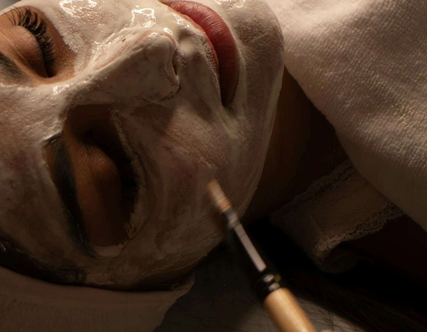 Editorial close-up of a facial mask being applied with a brush